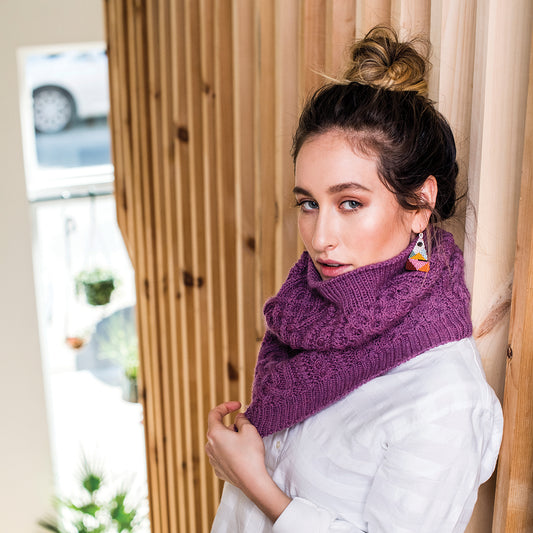A Chinese American female wearing the heavily cabled Compass cowl in orchid heather pink.