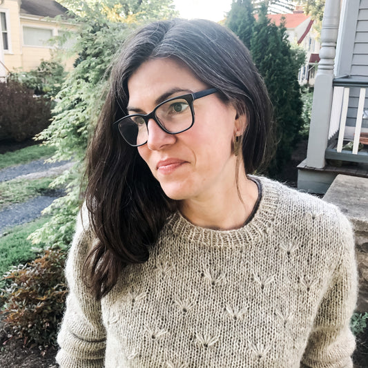 Close up of white model with brown hair standing outside wearing a Navia Brushed Tradition sweater, the Dandelion pattern by Sara J Mrdalo
