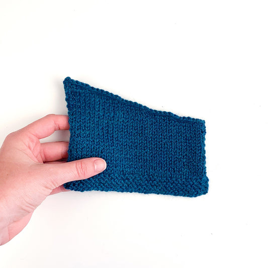 Hand holding a teal green swatch finished with a sloped bind off.